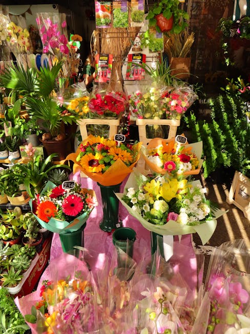 A vibrant display of fresh floral bouquets arranged on pink fabric-covered tables inside a florist shop. The bouquets feature a variety of colourful flowers including bright pink gerbera daisies, yell